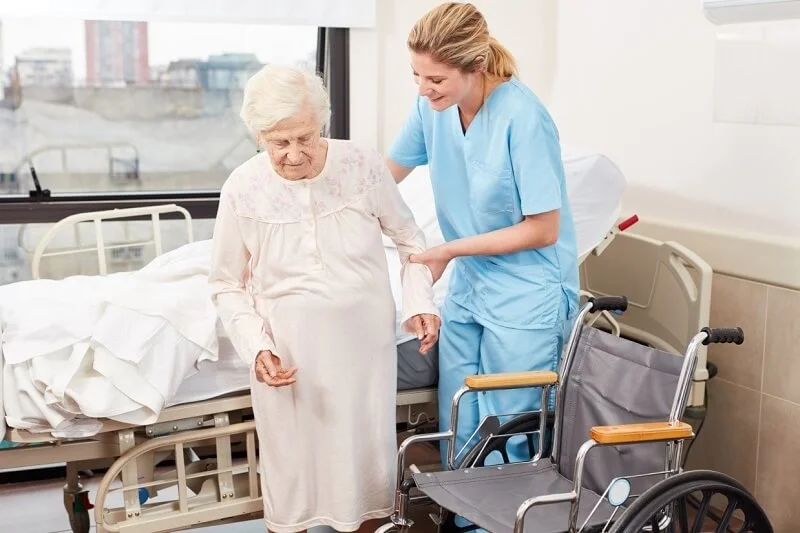 همراه بیمار در بیمارستان به خانم مسن کمک می کند بلند شود